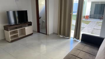 Sala de estar com televisão em suporte de madeira, porta que dá para uma varanda e vista para o exterior.