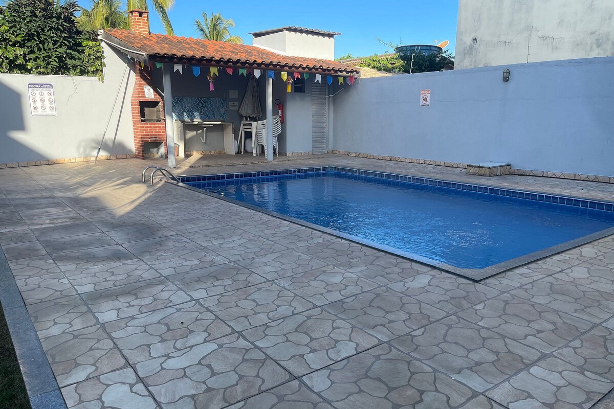 Ein Pool mit Steinfliesen, ein kleiner überdachter Bereich mit Stühlen und eine Wand mit einem Schild.
