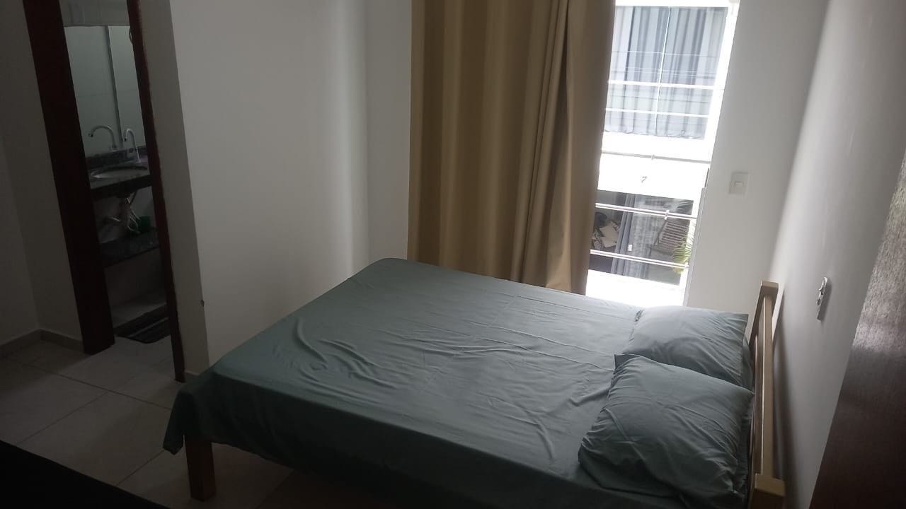 A single bed with a green bedspread in a room with a window, a door, and a mirror.
