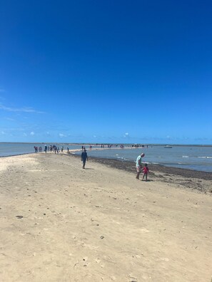 Ein Strand mit Menschen, die gehen und stehen, einem klaren Himmel und einem entfernten Steg.