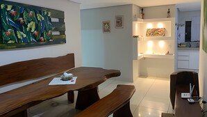 A dining area with a wooden table and benches, a painting on the wall, and a kitchen area with white cabinets and a countertop.