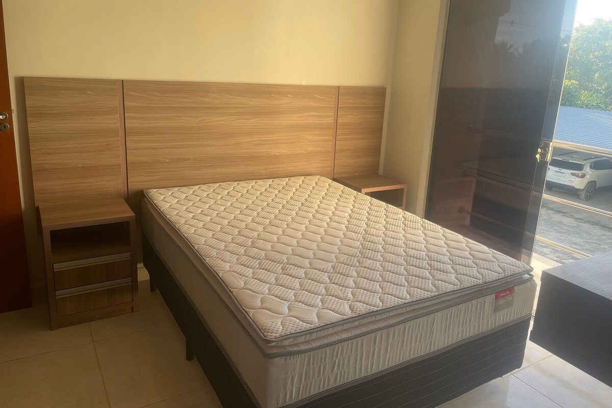 Ein Schlafzimmer mit einem großen Bett, einem Holzkopfende, einem kleinen Nachttisch und einer Schiebetür zum Balkon.