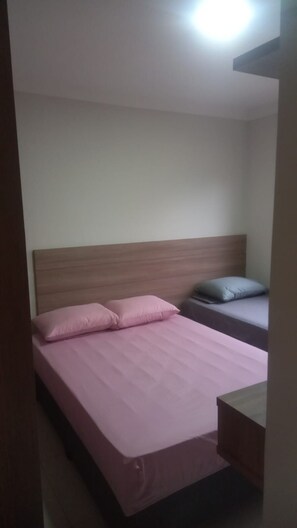 A single bed with a wooden headboard, a bedside table, and a nightstand. - Residencial Brasil Coroa (Santa Cruz Cabrália)