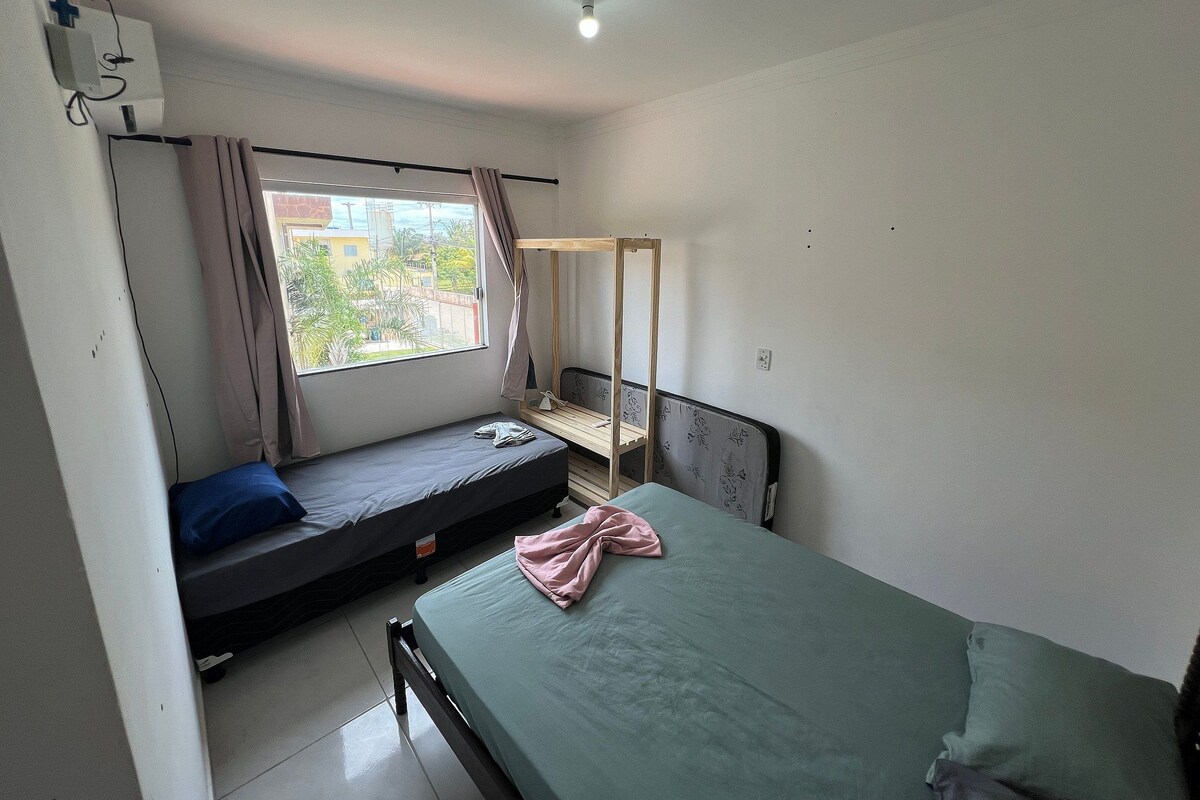 Ein Schlafsaalzimmer mit zwei Betten, einem fenster mit Vorhängen, einer Deckenleuchte und einer Steckdose an der Wand.