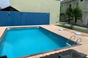 Ein rechteckiger Pool mit blauer Innenseite, umgeben von einer gefliesten Liegefläche und einer niedrigen Mauer.