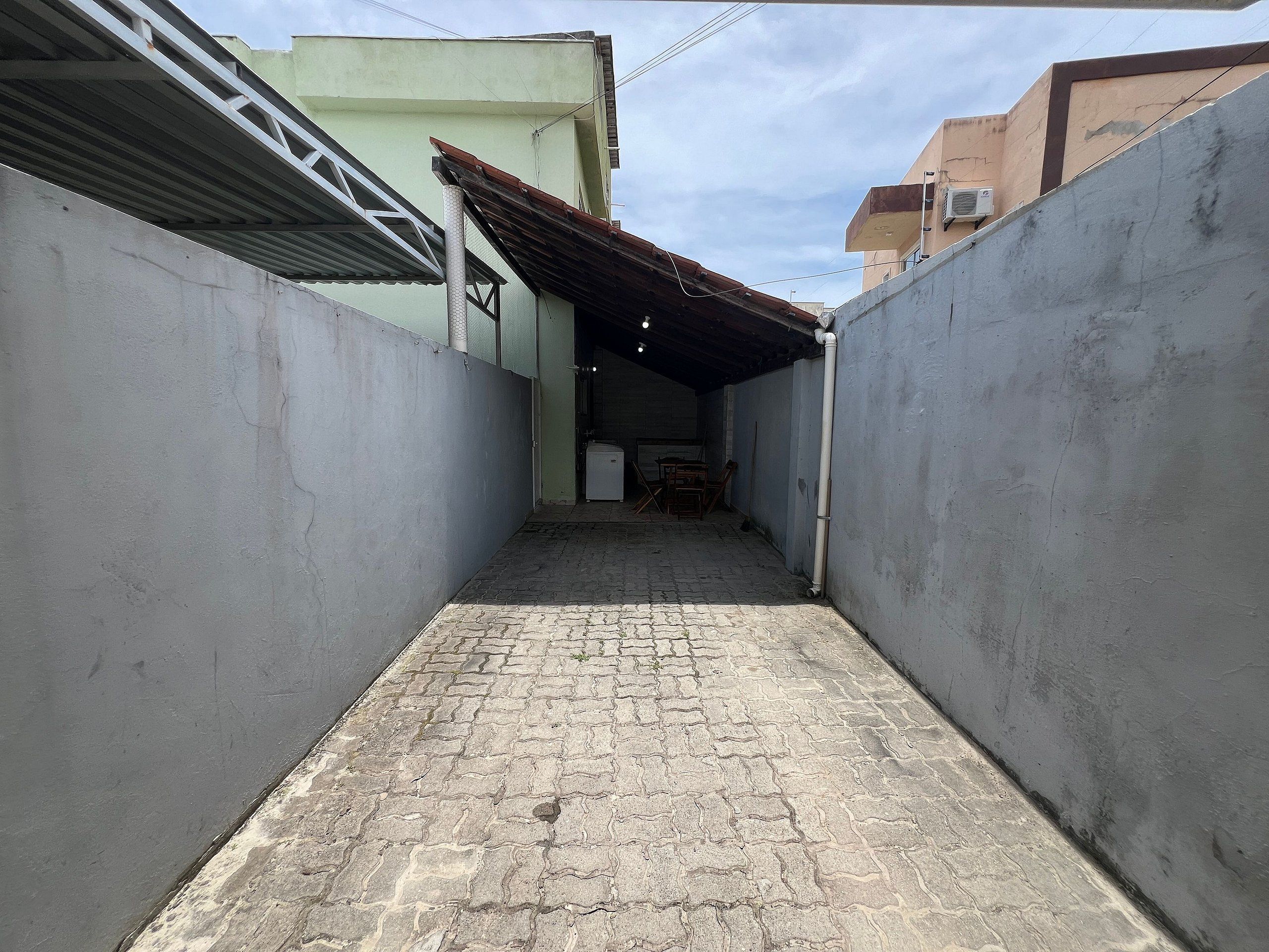Un estrecho callejón con un camino adoquinado, flanqueado por edificios con paredes de concreto y techos de metal.