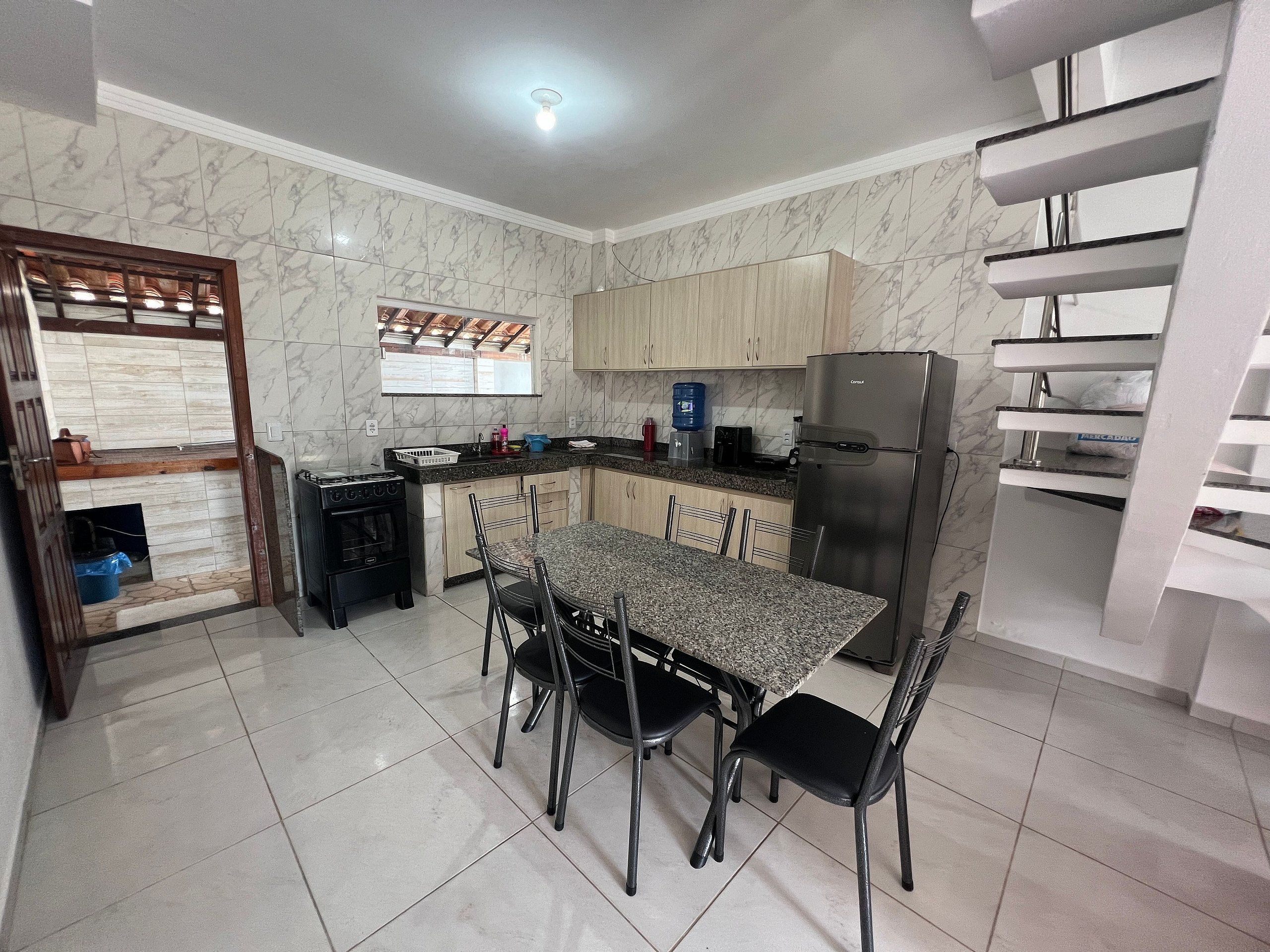 Uma cozinha com mesa de jantar, cadeiras, geladeira e uma janela.