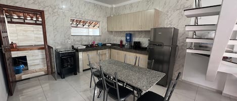 A kitchen with a dining table, chairs, a refrigerator, and a window.