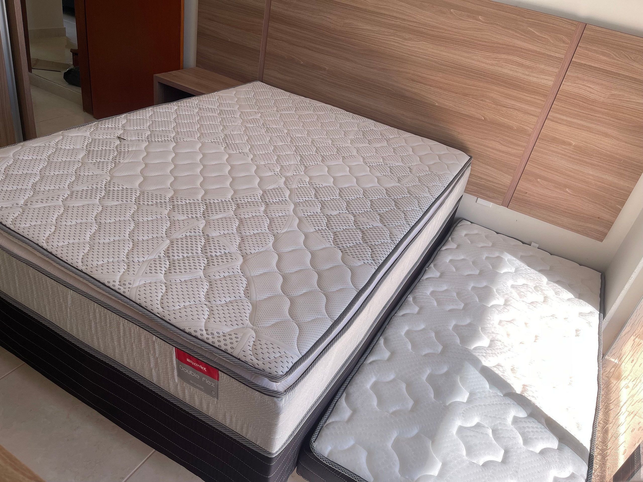 A double mattress in a room with wooden headboard and a tiled floor.