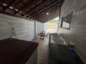 Un área de cocina al aire libre con techo, una mesa de comedor y sillas, un lavamanos y una mesa de madera.