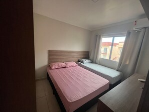 Ein Schlafzimmer mit Bett, einem Fenster mit Vorhängen, einer Tür und Blick auf Gebäude.