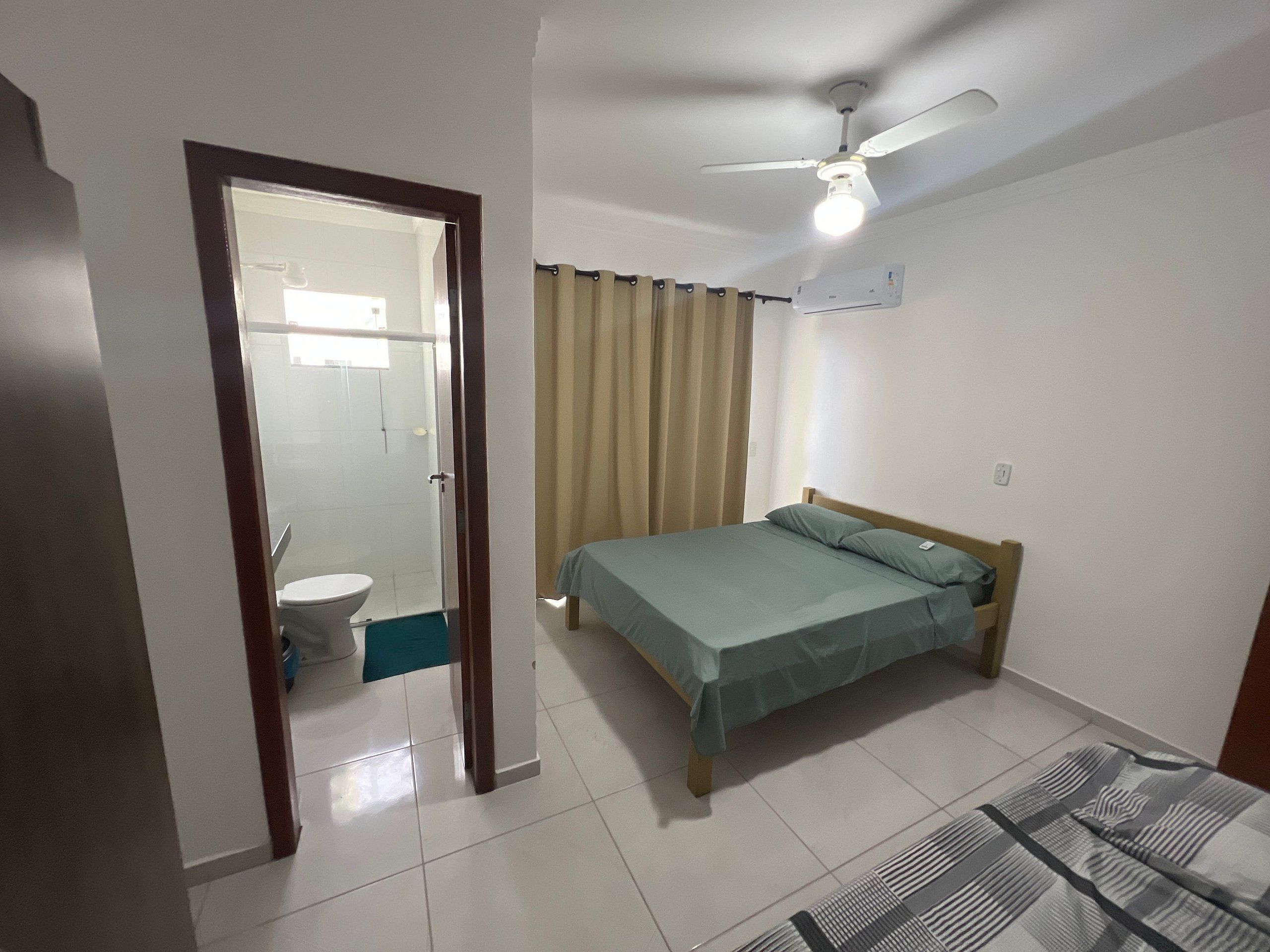 A bedroom with a bed, a ceiling fan, a window with curtains, and a bathroom visible through an open door.