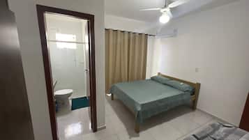 A bedroom with a bed, a ceiling fan, a window with curtains, and a bathroom visible through an open door.