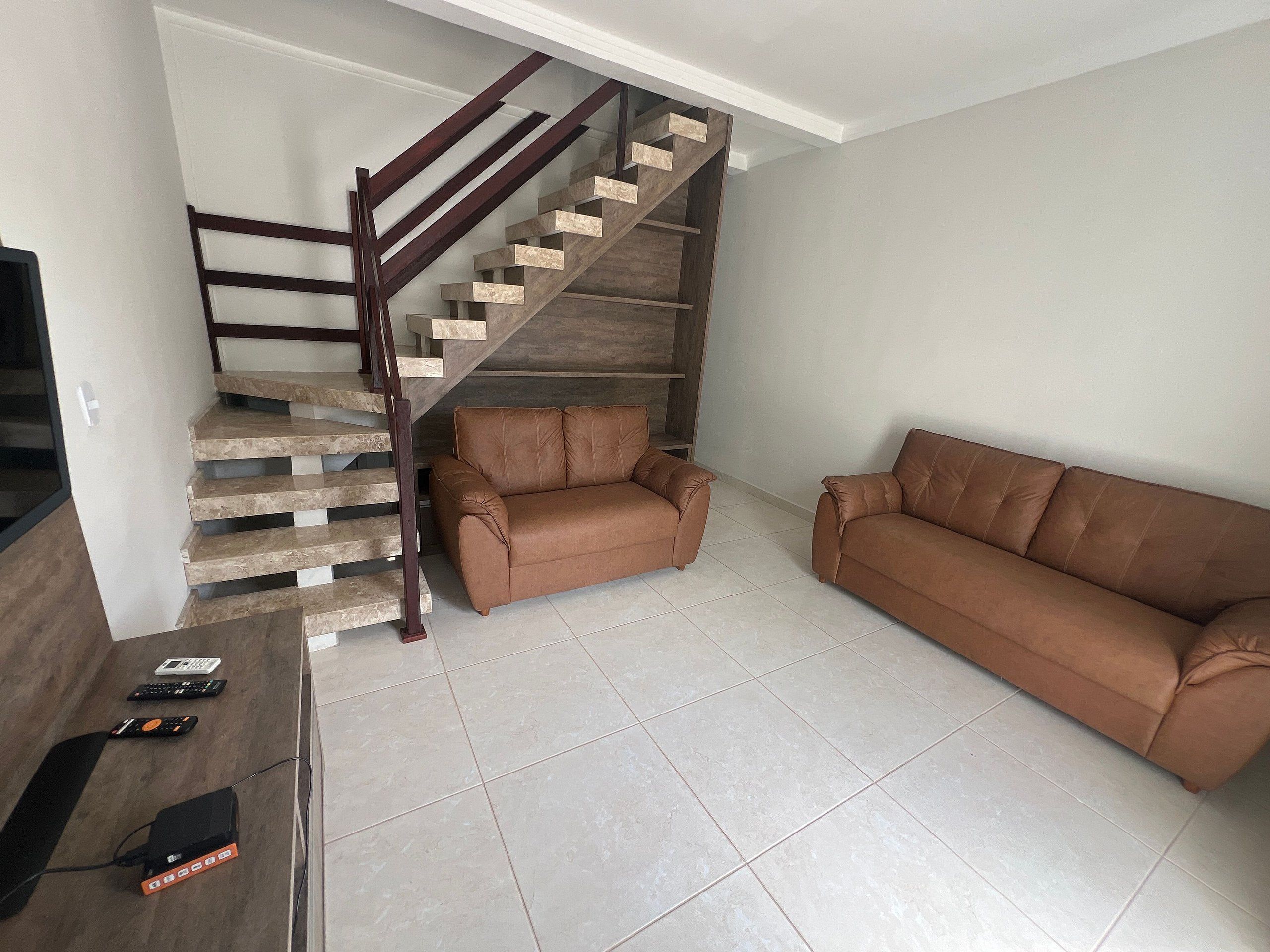 Una sala de estar con una escalera, un sofá de cuero marrón y un televisor de pantalla plana.