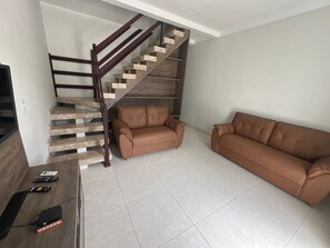 Ein Wohnzimmer mit Treppe, einem braunen Ledersofa und einem Flachbildfernseher.