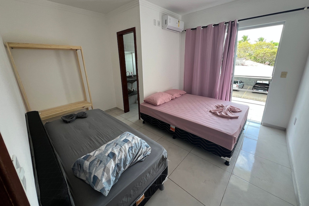 Ein Schlafzimmer mit Bett, Stuhl, Spiegel, Fenster mit Vorhängen und Blick nach draußen.
