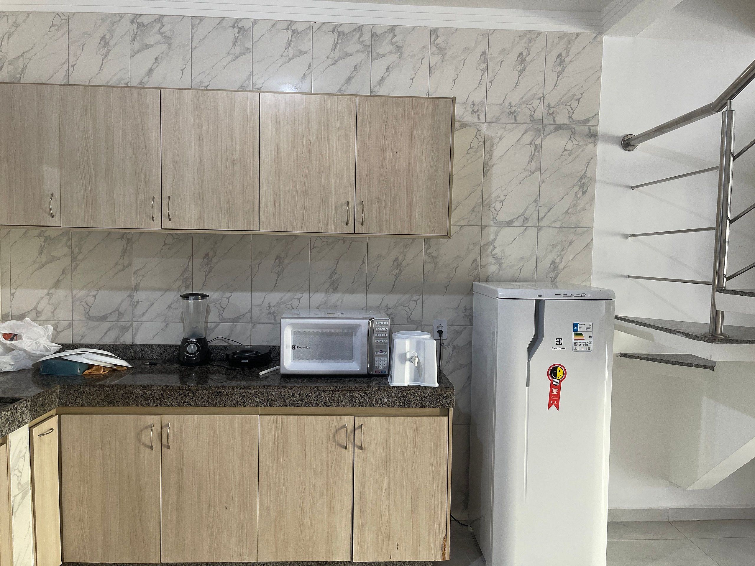 Una cocina con baldosas de mármol, armarios de madera, microondas y refrigerador.