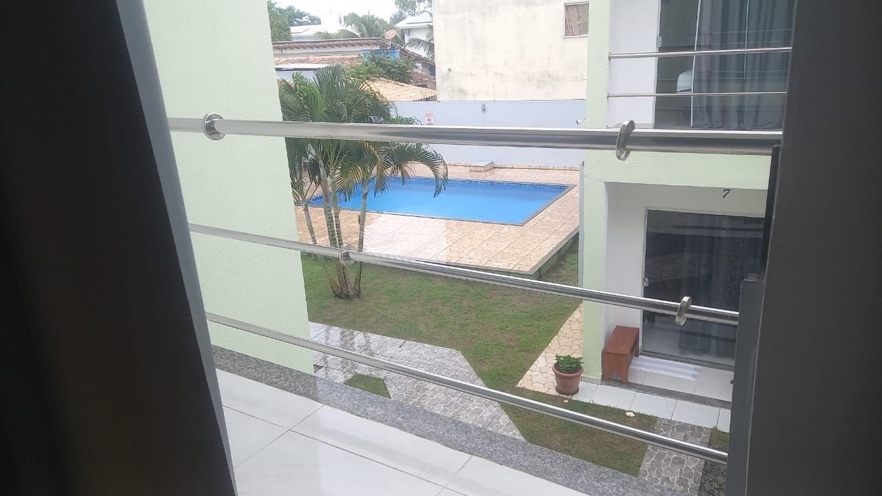 Un balcon avec une rambarde en métal, une petite plante en pot et une vue sur une piscine et les bâtiments adjacents.