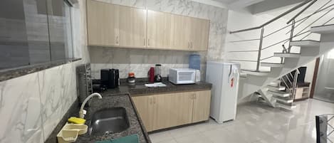 Cozinha moderna com painel de mármore, armários de madeira, bancada de granito, cuba de aço inoxidável e micro-ondas embutido.