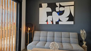 A modern living room with a grey sofa, a wooden coffee table, and a large abstract painting on the wall. - Mat Suites (rhodes)