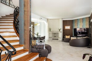 A modern living room with a wooden staircase, a fireplace, a television, and a seating area.