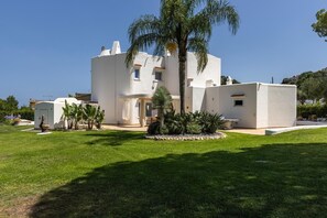 A modern white building with a flat roof, surrounded by a well-maintained lawn and palm trees.