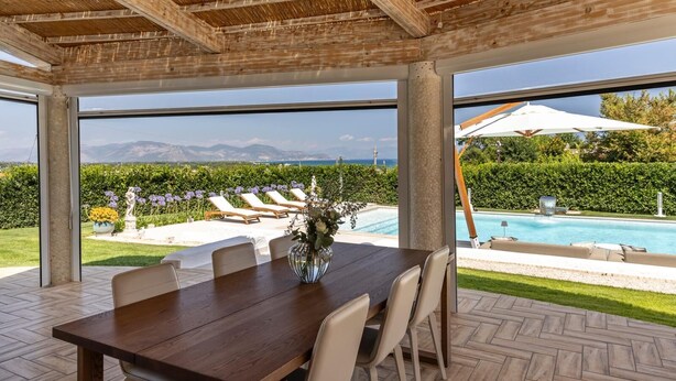 A covered outdoor dining area with a view of a pool and mountains.