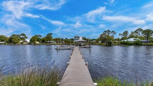 A wooden pier leading to a house with a covered area, surrounded by water and trees. - 1BR Studio with Pool & Dock, Steps from the Beach! (Panama City Beach)
