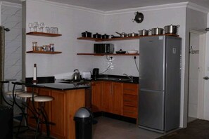 Una cocina compacta con armarios de madera, un refrigerador de acero inoxidable y un microondas en un estante.