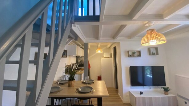 Ein modernes Interieur mit Treppe, Essbereich mit Tisch und Stühlen, Flachbildfernseher und einer hängenden Pendelleuchte.