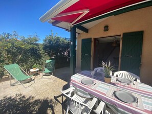Un patio con una mesa lista para dos personas, dos sillas, una mesita auxiliar y una planta en maceta.