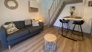 Ein modernes Wohnzimmer mit einer Couch, einem runden Couchtisch und einer Treppe, die in einen Essbereich mit Barhocker führt.