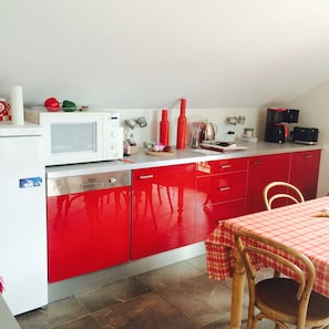 A kitchen with a red and white color scheme, a microwave, a coffee maker, and a table with a checkered tablecloth. - Available August 8–15! Chamonix, large apartment facing Mont Blanc, exceptional view, sleeps 4 (Chamonix-Mont-Blanc)