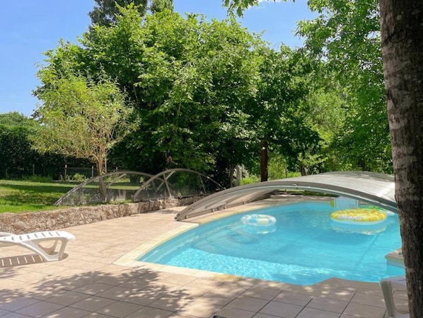 Une piscine dotée d’un espace couvert, entourée d’arbres et baignée par un ciel dégagé.