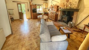A living room with a sofa, fireplace, kitchen, and wooden beams. - Charming cottage near Loire Castles (La Chapelle-Montmartin)