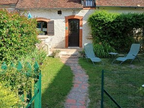 Une maison avec un chemin de pierre menant à une porte, deux chaises de jardin et une clôture verte.