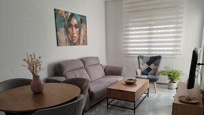 Een moderne woonkamer met een bank, een eettafel, stoelen, een salontafel, een schilderij, een potplant en een televisie.