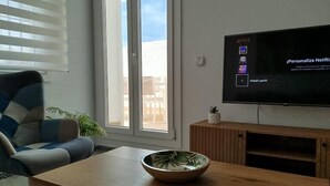 Een woonkamer met een televisie, een bank, een salontafel en een schuifdeur van glas.