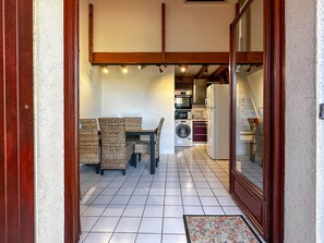Een kleine keuken met een wasmachine, een koelkast en een eethoek met rieten stoelen.