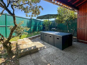 Un espace patio avec un jacuzzi, une pergola dotée d’un parasol et une clôture verte.
