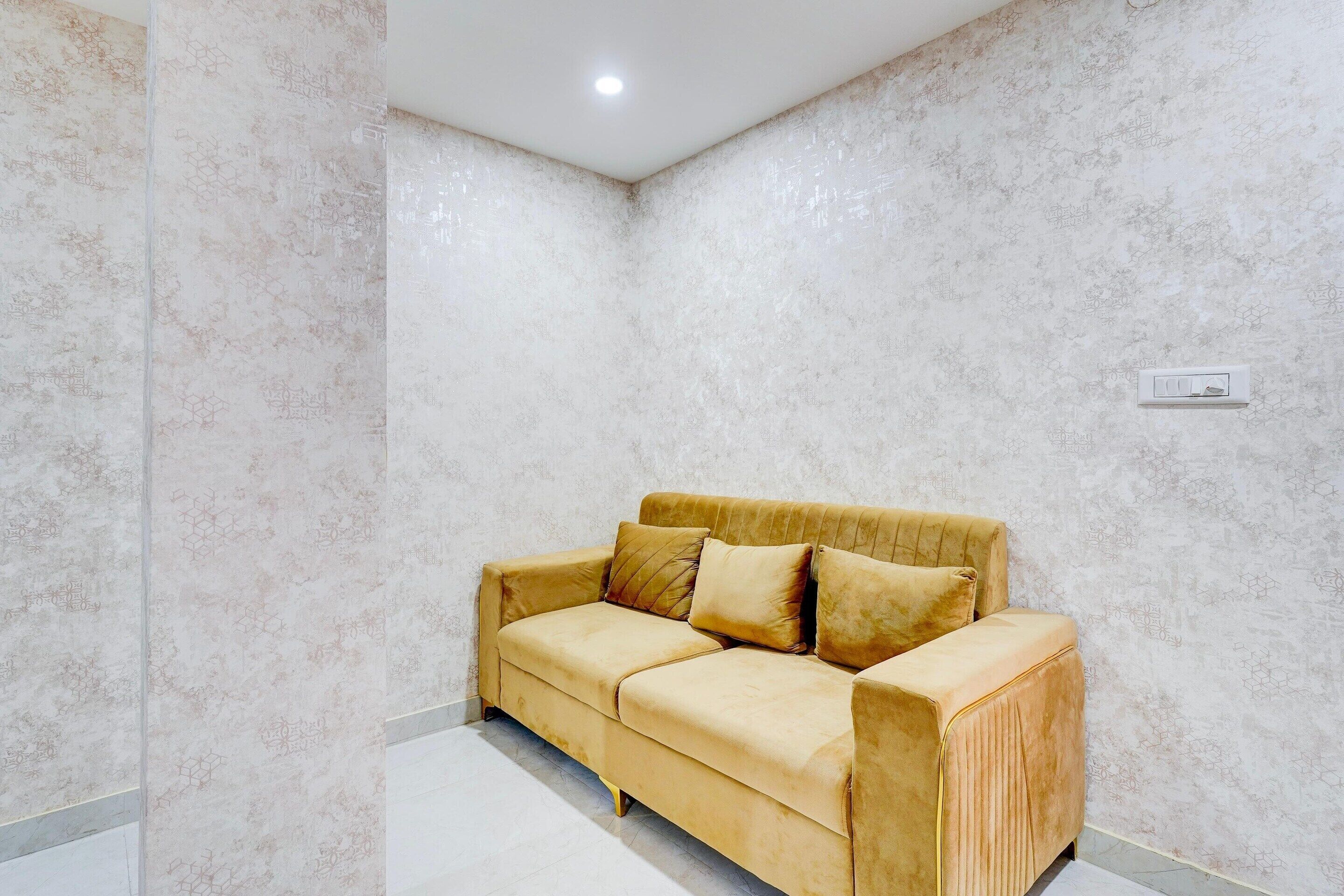 Un canapé beige placé dans un coin, avec des murs à motifs et un luminaire au plafond.
