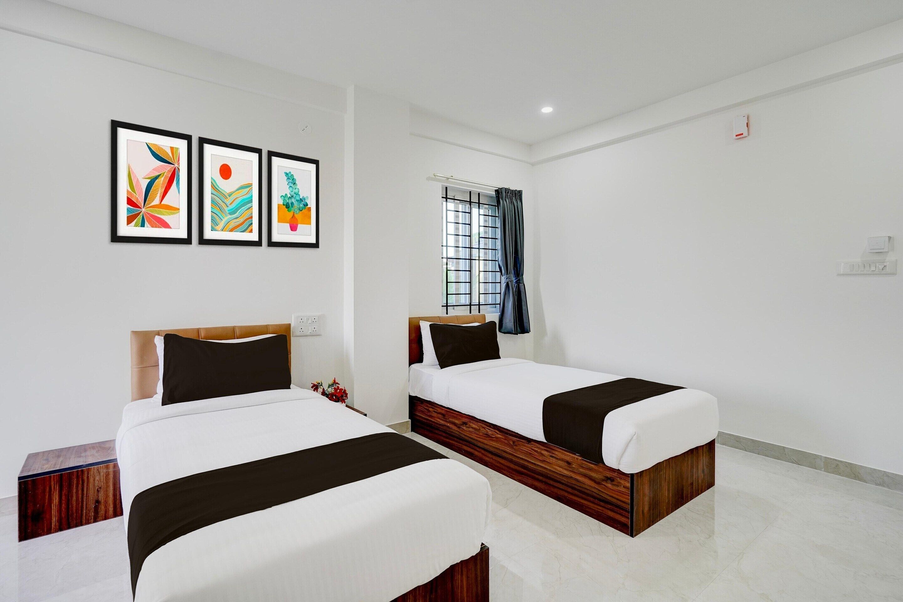 A hotel room with two beds, a window with curtains, and three framed artworks on the wall.