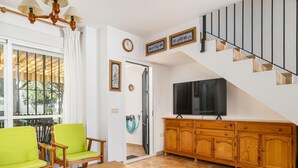 Un salon avec un meuble TV en bois, un canapé, une table basse, un escalier et une vue par la fenêtre.