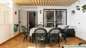 Une terrasse dotée d’un plafond à rayures, d’une table avec des chaises et d’une vue sur l’extérieur, visible à travers une fenêtre.