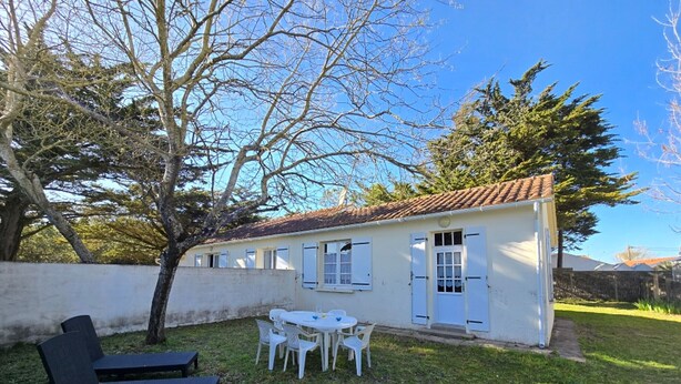 A white building with a tiled roof, a patio with a table and chairs, and a black lounge chair. - Quiet holiday house near the sea - 4 guests (Saint-Hilaire-de-Riez)