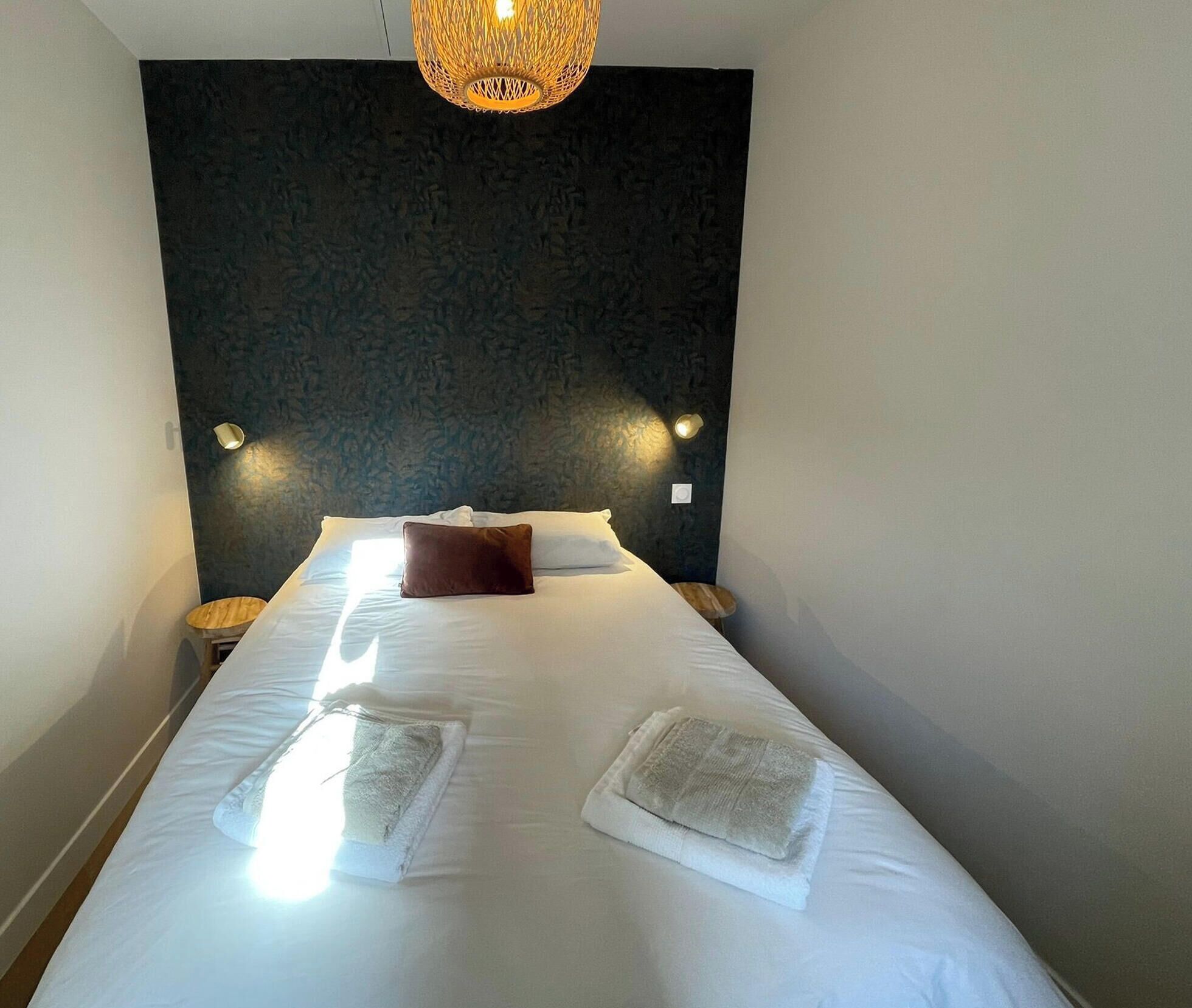 A hotel room with a large bed, two bedside lamps, a textured dark wall, and a hanging light fixture.
