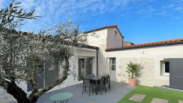 A building with a patio area, a table with chairs, and a potted plant. - House with AC and parking - 6 guests (Saint-Vincent-Sterlanges)