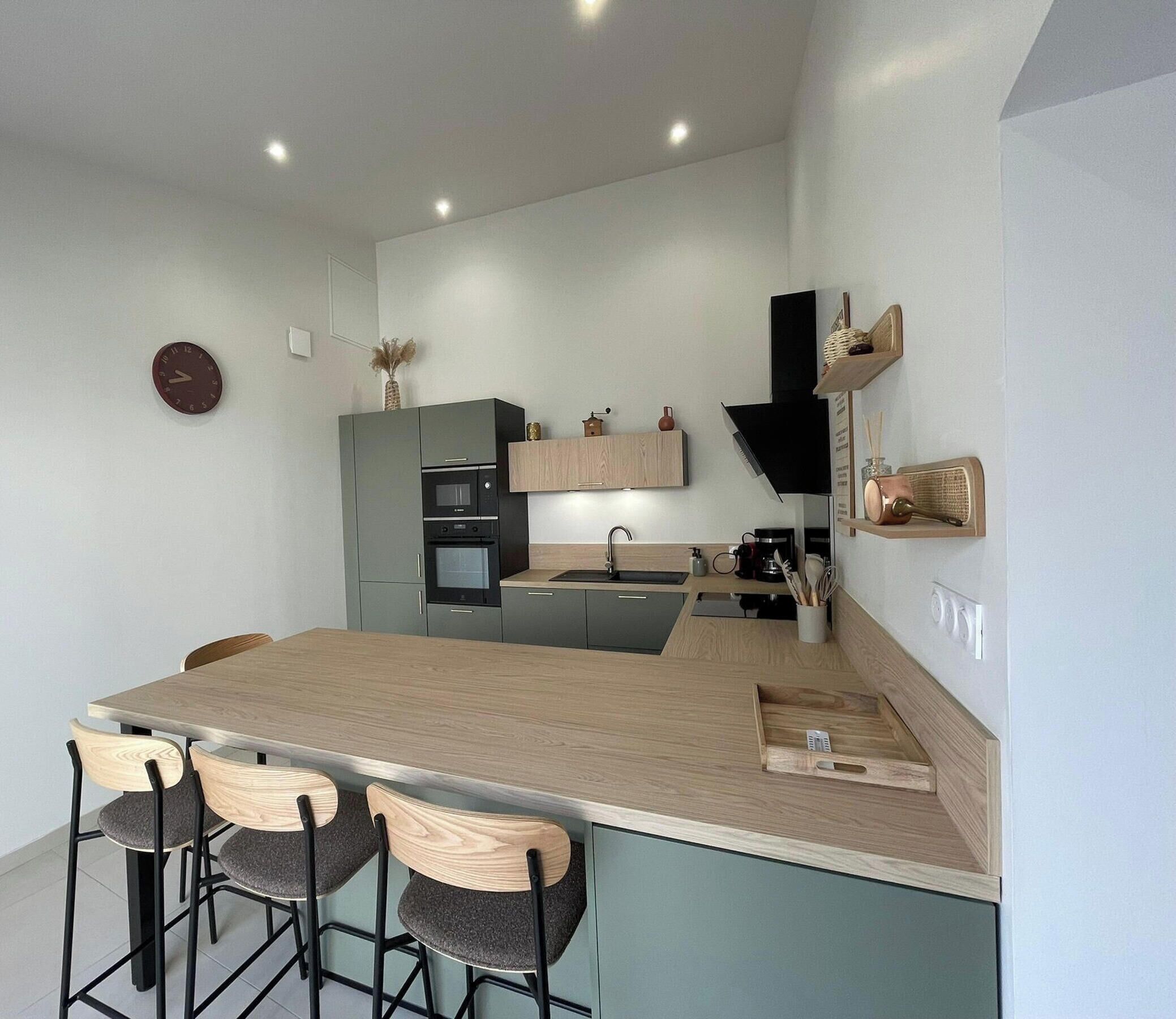 Eine moderne Küche mit Kochinsel, Barhocker, integrierten Geräten und einer Holzrückwand.