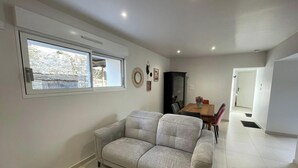 A living room with a sofa, a dining table with chairs, a black cabinet, and a window with a view of a stone wall. - House with AC and parking - 6 guests (Saint-Vincent-Sterlanges)