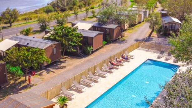 A poolside view of a resort with individual cabins, a clear blue pool, and a view of the sea. - Mobile home with AC - Pets OK - 6 guests (Frontignan)